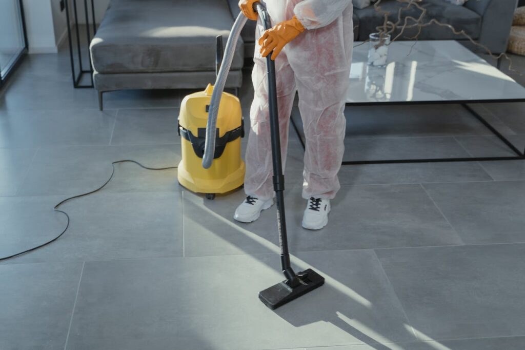 pexels photo 6195949 A professional cleaner in protective gear vacuuming the floor in a modern living room.